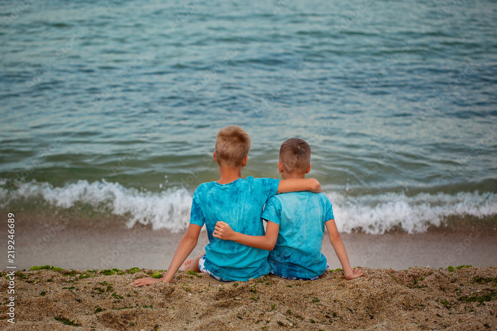 Two brothers sitting on sea beach in summer day. Back view Two brothers sitting on sea beach in summer day. Back view