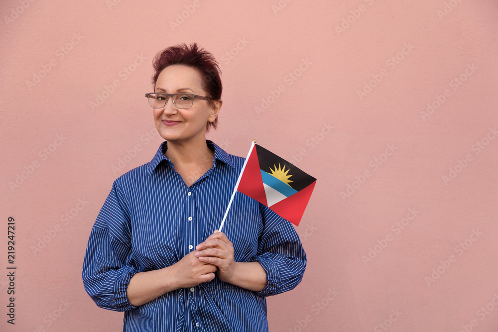 Antigua and Barbuda flag. Woman holding Antigua and Barbuda flag. Nice portrait of middle aged lady 40 50 years old with a national flag over pink wall on the street. Visit Caribbean islands Antigua and Barbuda flag. Woman holding Antigua and Barbuda flag. Nice portrait of middle aged lady 40 50 years old with a national flag over pink wall on the street. Visit Caribbean islands
