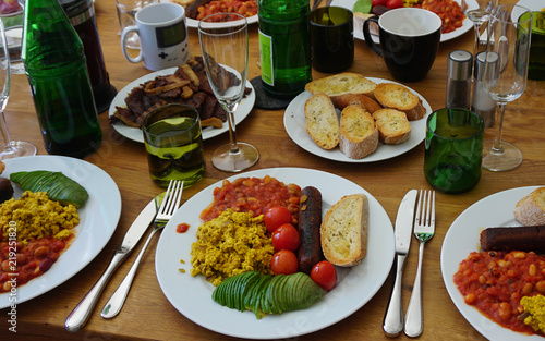 Full vegan english breakfast with vegan chorizo sausages, vegan seitan bacon, scrambled tofu eggs, avocado, baked beans, roasted tomatoes and bread