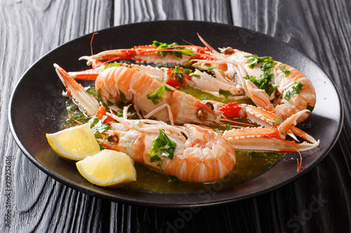 Freshly cooked langoustines, scampi with lemon and tasty sauce with herbs close-up on a plate on a black table. horizontal