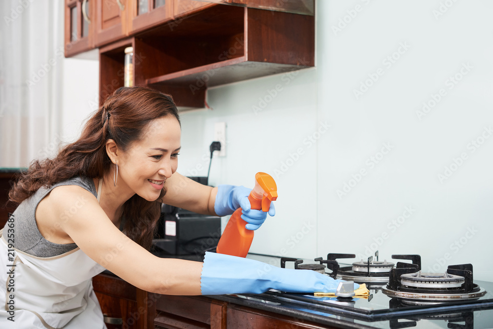 Housewife spraying stove with detergent before wiping it Housewife spraying stove with detergent before wiping it