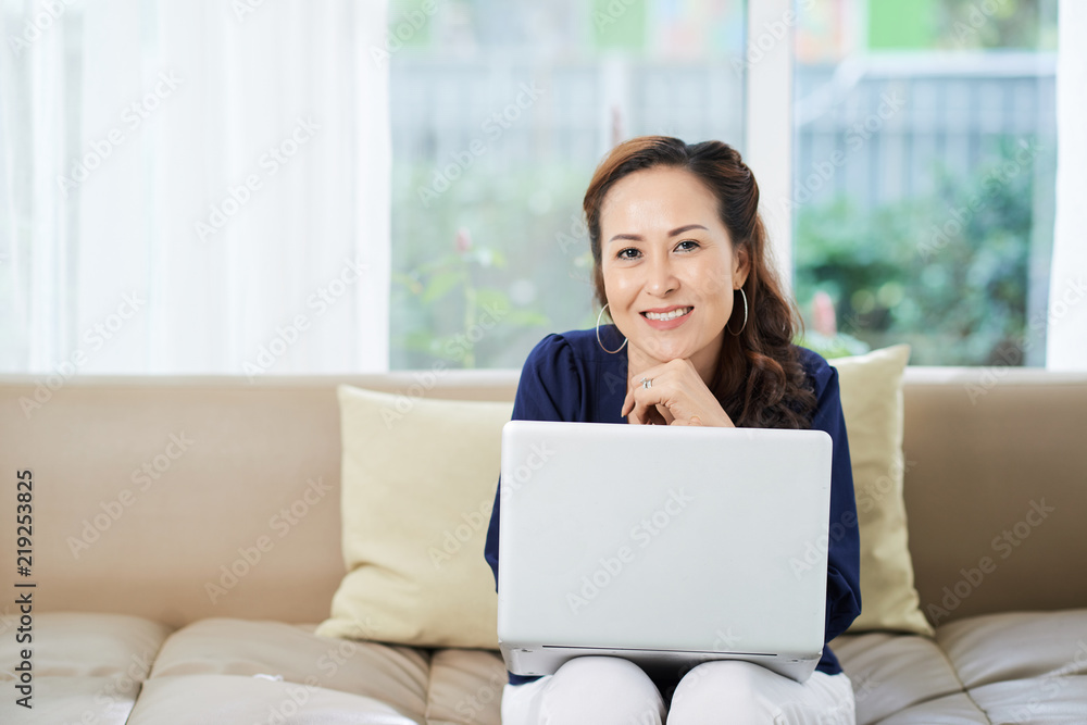 Portrait of pretty smiling woman sitting on couch with laptop on her laps Portrait of pretty smiling woman sitting on couch with laptop on her laps