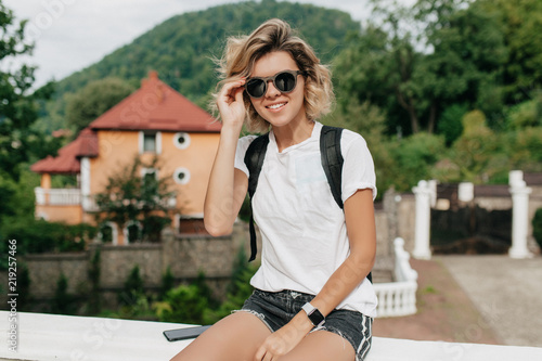 Female traveler hipster with backpack  in sunglasses smilimg to camera and looking forward at amazing mountains and valley view. Space for text. Travel concept photo