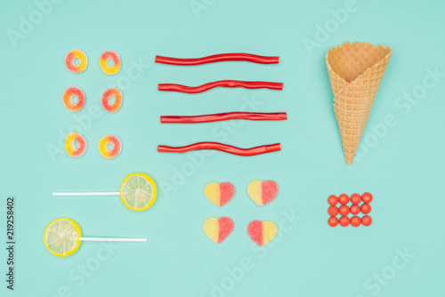 flat lay of jelly candies, dragee, lollipops and waffle cone isolated on turquoise photo