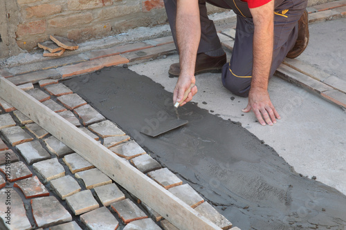 Old tiles recycling, making terrace or pavement using tile pieces, workers hand spreading mortar or tile adhesive using trowel