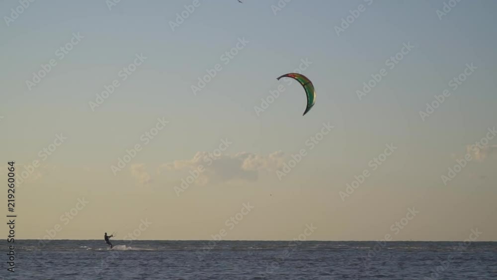 A man in the windy afternoon engage kitesurfing at sea, birds fly across the sky A man in the windy afternoon engage kitesurfing at sea, birds fly across the sky