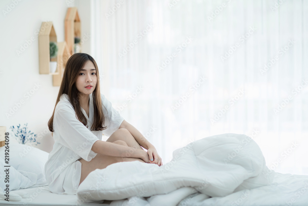 Beautiful Asian lady resting on white bed. Cute women sitting in the bed her smile thinking about something. Beautiful Asian lady resting on white bed. Cute women sitting in the bed her smile thinking about something.
