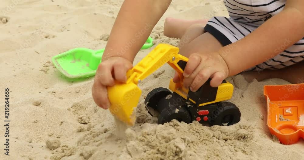 Crop kid playing raod works with toy excavatorin in a sand pit Crop kid playing raod works with toy excavatorin in a sand pit