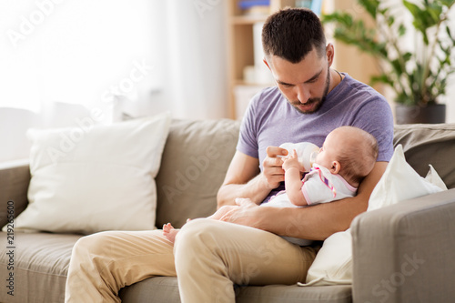 family, parenthood and people concept - father feeding little daughter with baby formula from bottle at home