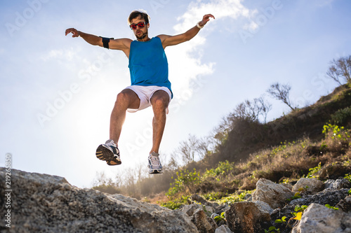 bottom view of athletic man jumping from rocks with sunlight