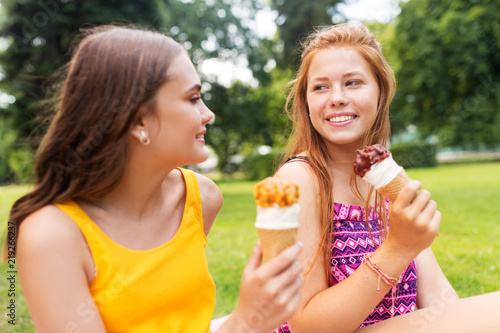 leisure and friendship concept - happy smiling teenage girls or friends eating ice cream at picnic in summer park