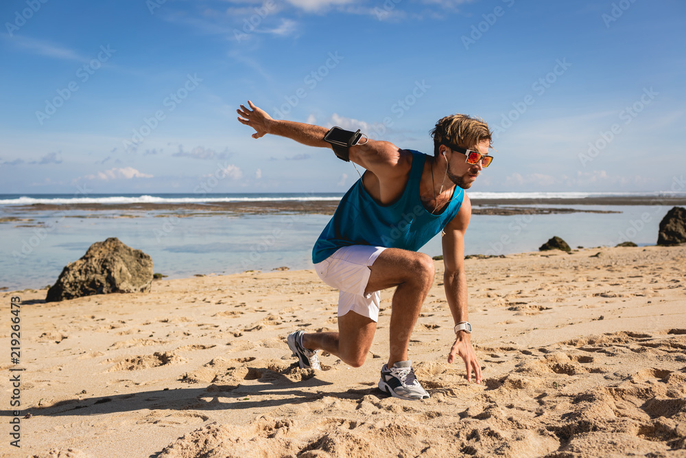 athletic handsome man doing lunges during workout on seashore