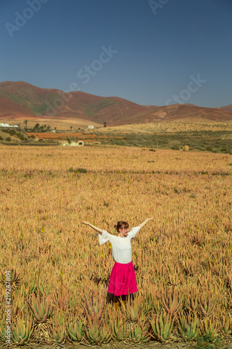 Young happy woman standing with open arms in aloe vera field in Fuerteventura.