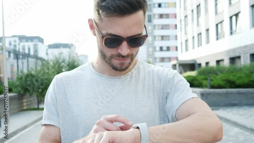 Handsome stylish young man using smartwatch. Man walking on the street and making various gestures with a finger on a touch screen of a smart watch. photo