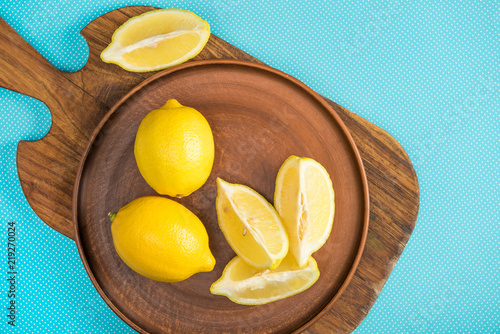top view of yellow lemons in ceramic plate on wooden cutting board on turquoise