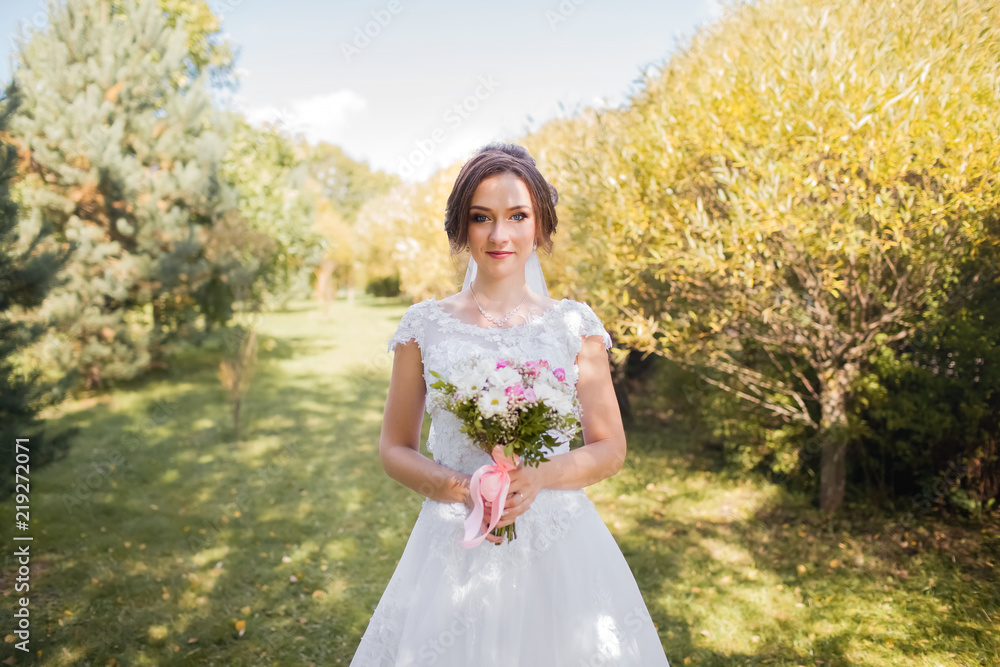 Beautiful bride with bridal bouquet. Portrait of a woman in white wedding dress in the autumn park