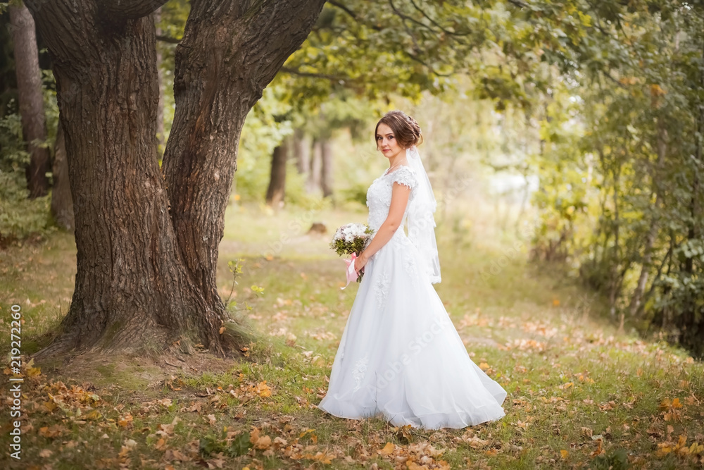 Beautiful bride with bridal bouquet. Attractive woman walks in the autumn park in white wedding dress