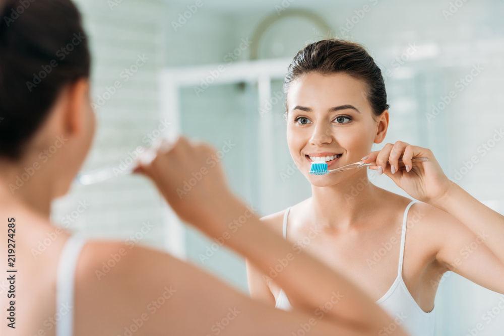 beautiful smiling girl brushing teeth at mirror in bathroom beautiful smiling girl brushing teeth at mirror in bathroom