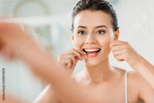 Quadro su tela selective focus of beautiful smiling girl using dental floss in bathroom