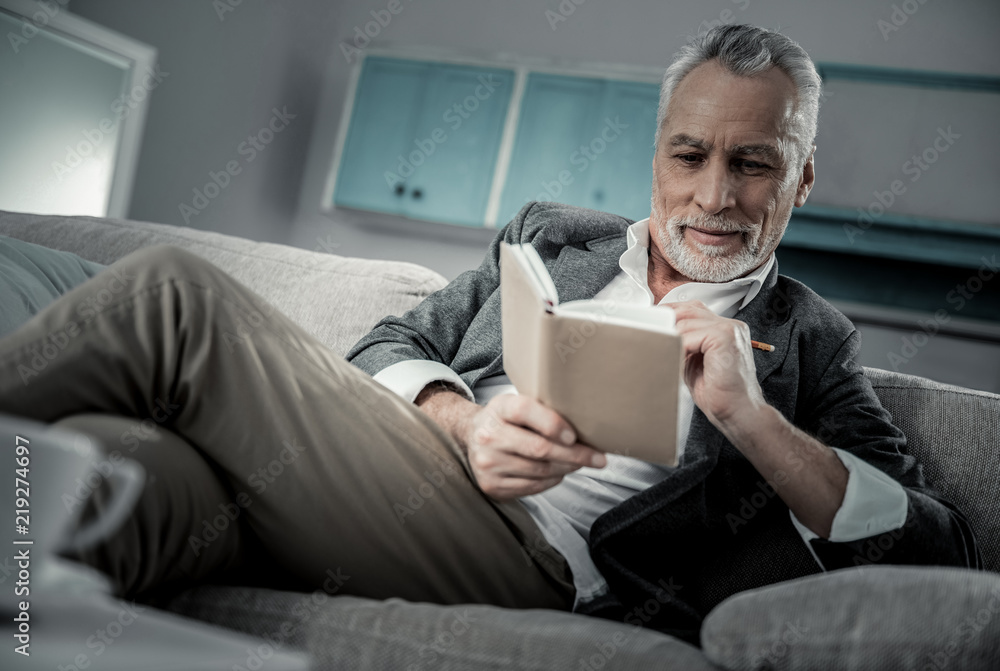 Casual style. Attentive bearded mature man sitting on the sofa while looking at his notebook