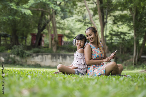 Mother and daughter reading a fairytale to her daughter listen sound with headphone in the park © Johnstocker