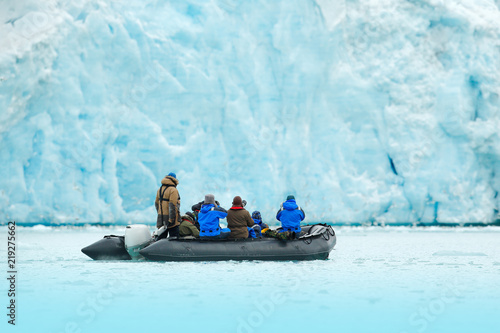 Nature lovers in Arctic Svalbard, Norway. Motor boat with tourists on the ice sea with glacier. Arctic cruise in winter, black powerboat with photographers, snowy icebreaker in background.