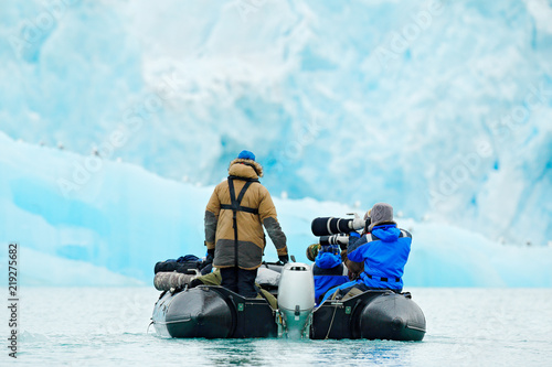 Nature lovers in Arctic Svalbard, Norway. Motor boat with tourists on the ice sea, snowy mountain in background. Arctic cruise in winter, black powerboat with photographers.