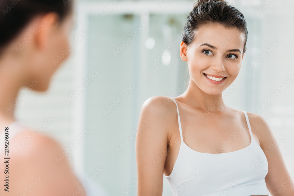 beautiful smiling brunette girl in underwear looking at mirror in bathroom