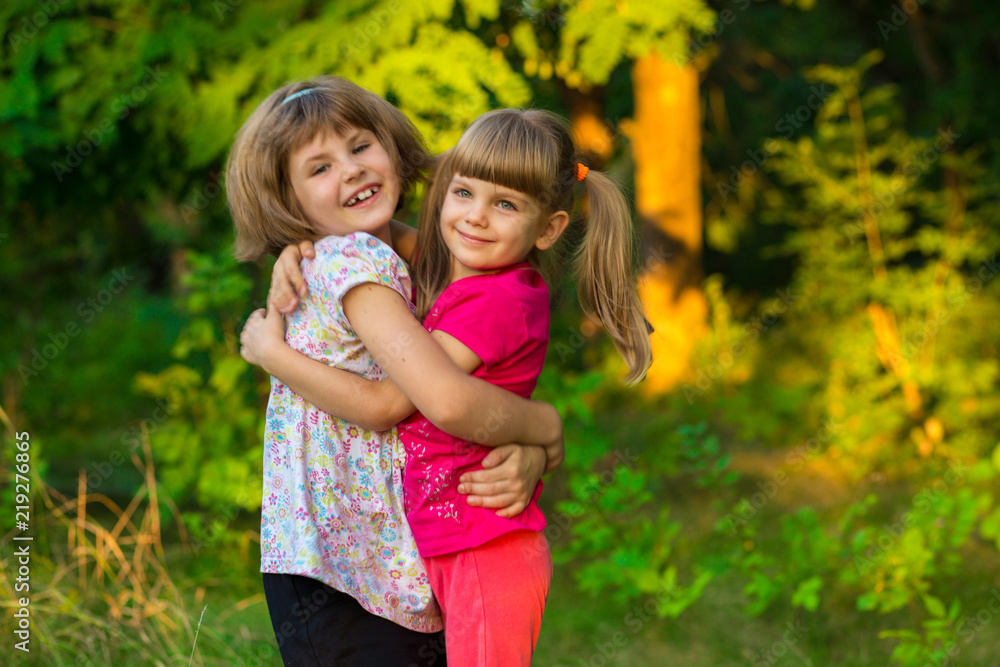 Two adorable little sisters laughing and hugging on sunny day in summer park Two adorable little sisters laughing and hugging on sunny day in summer park