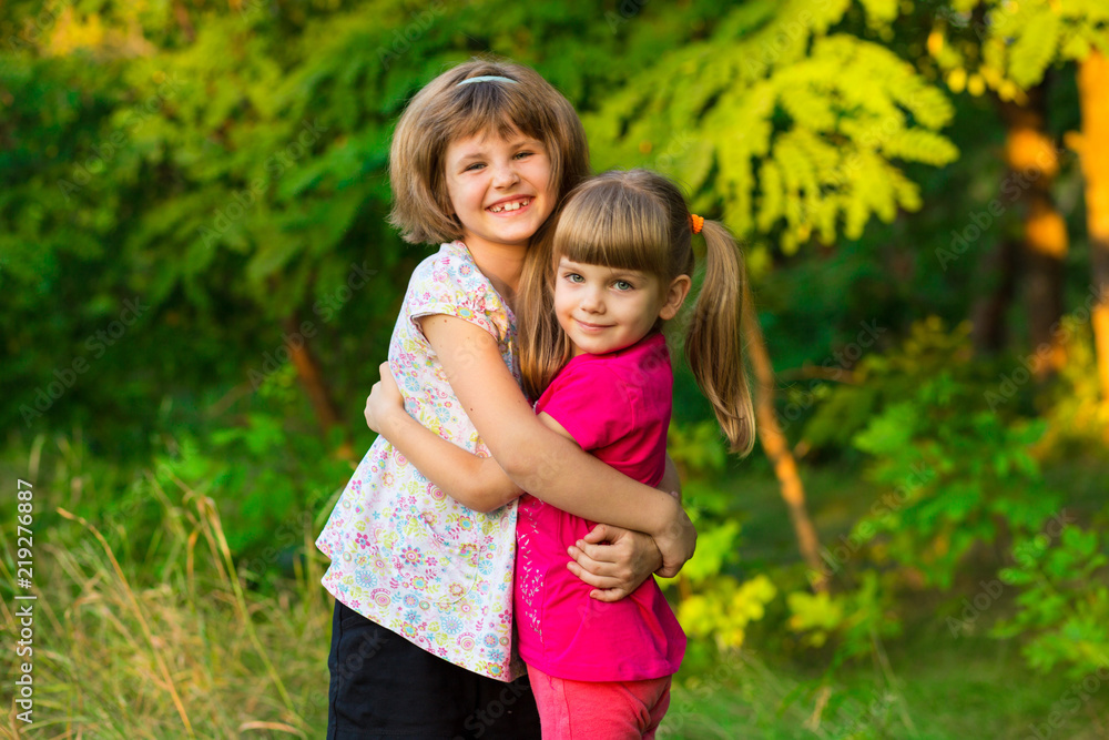 Two adorable little sisters laughing and hugging on sunny day in summer park Two adorable little sisters laughing and hugging on sunny day in summer park