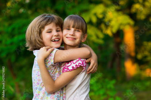 Two adorable little sisters laughing and hugging on sunny day in summer park