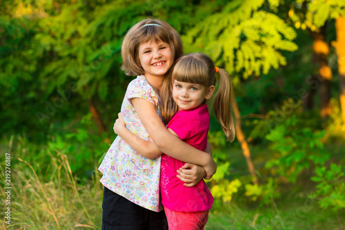 Two adorable little sisters laughing and hugging on sunny day in summer park