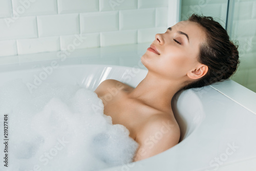 beautiful young woman with closed eyes relaxing in bathtub with foam