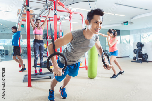 Cheerful fit young man exercising with gymnastic rings during routine workout in a trendy fitness center with modern equipment for functional training