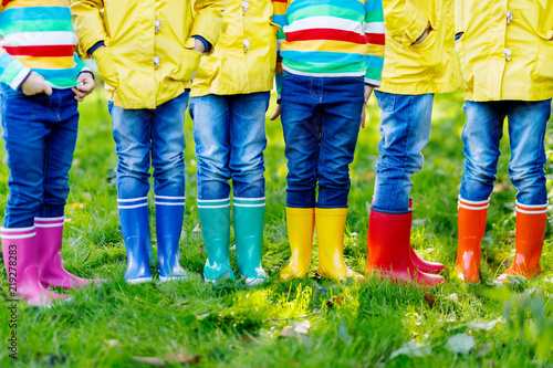 Little kids, boys and girls in colorful rain boots. Close-up of children in different rubber boots, jeans and jackets. Footwear for rainy fall