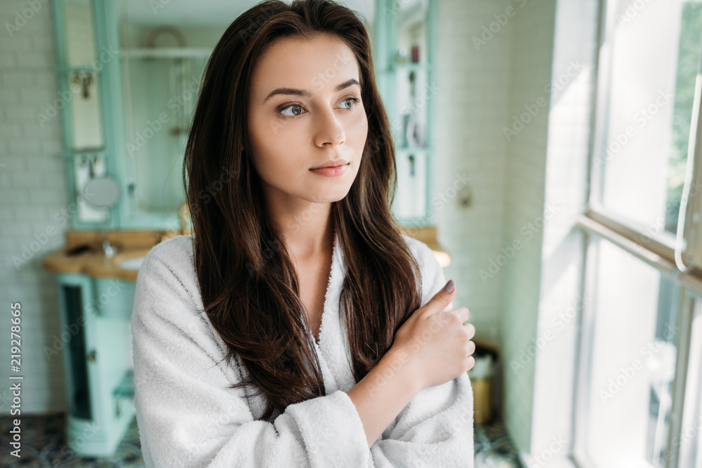 pensive brunette girl in bathrobe looking at window in bathroom pensive brunette girl in bathrobe looking at window in bathroom