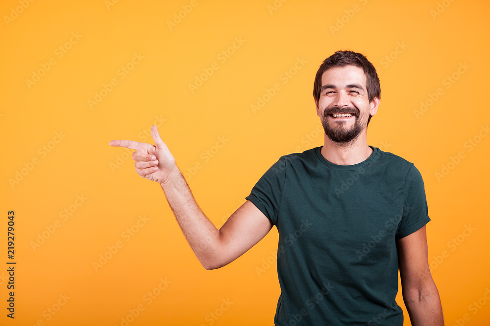 Cheerful smiling man pointing at his right at copyspace available for your advertisement or promotion. Isolated on orange backgorund in studio. Cheerful smiling man pointing at his right at copyspace available for your advertisement or promotion. Isolated on orange backgorund in studio.
