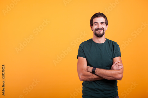 Handsome man with his arms crossed smiling at the camera isolated on yellow background. Portrait of attractive bearded confident person in studio photo