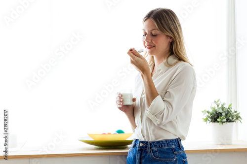 Beautiful young woman eating yogurt at home