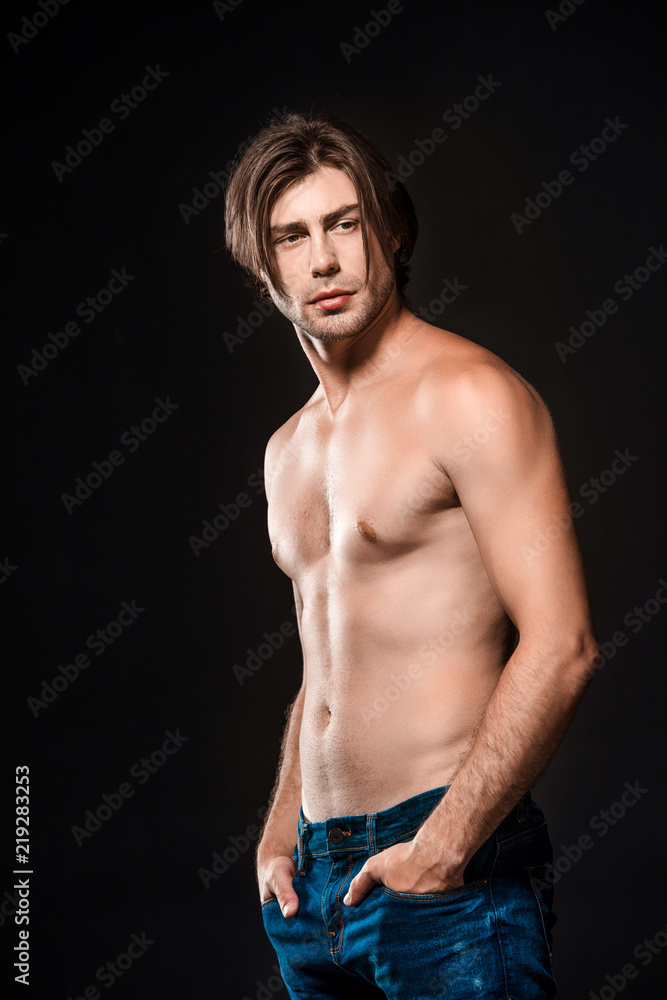 Fototapeta premium portrait of pensive shirtless man in jeans looking away isolated on black