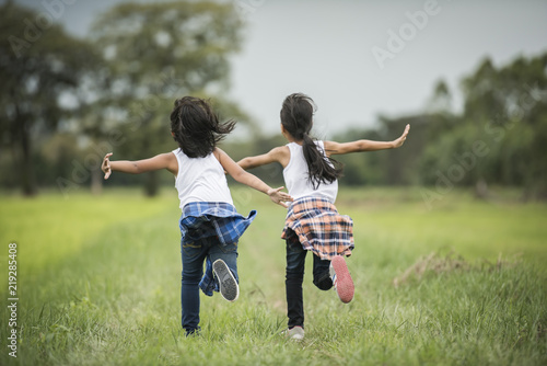 Two little cute girls are running on green grass. Best friends. photo