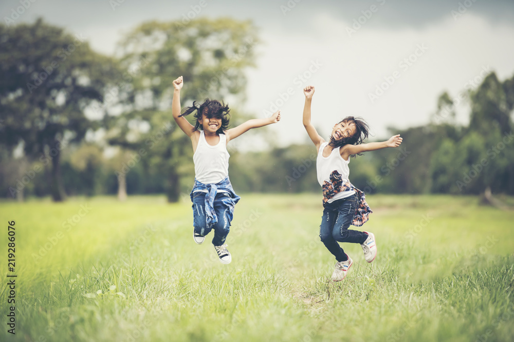Two little girls happy jump in the nature park Two little girls happy jump in the nature park