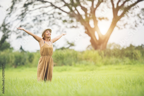 Young woman standing in grass field raising hands in the air.