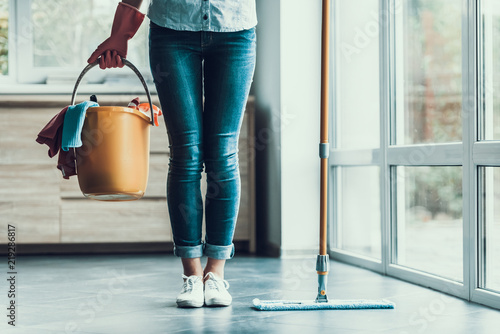 Young Woman holds Bucket with Cleaning Equipment