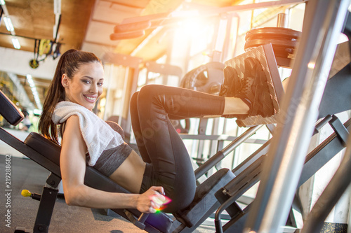 Sportive girl using weights machine for legs at the gym photo