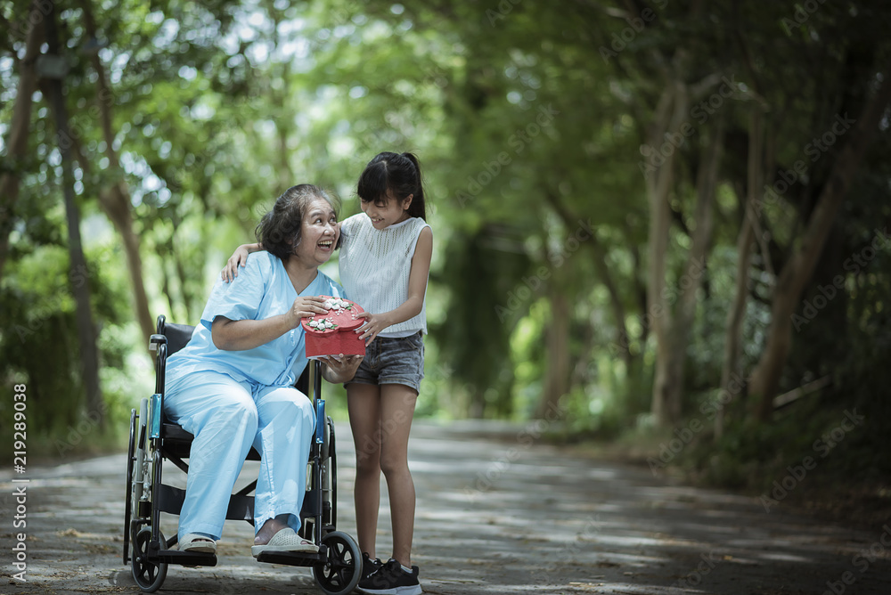 Asian senior or elderly old woman patient with happy and smile when get giving a gift from granddaughter visit on wheelchair in the hospital; mother's day concept. Asian senior or elderly old woman patient with happy and smile when get giving a gift from granddaughter visit on wheelchair in the hospital; mother's day concept.