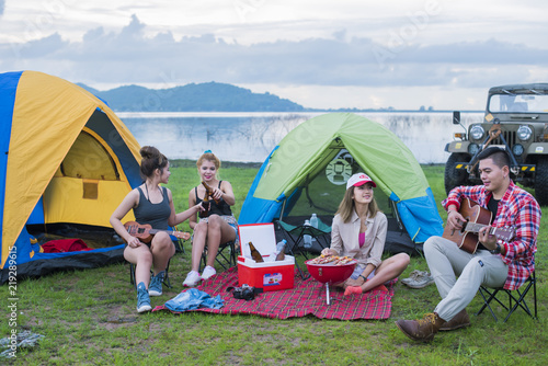 Group asian of man and women have friendship enjoy camping for picnic and barbecue at lake with tents on background; travel concept and happy familly.