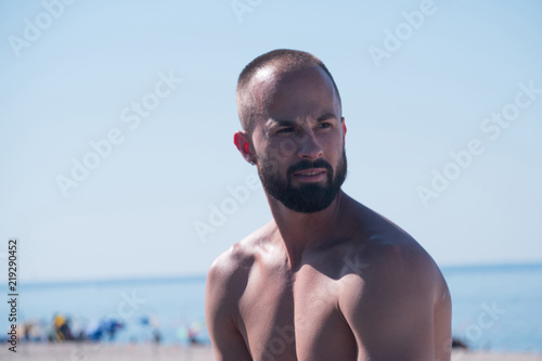 Side profile portrait photo of yong attractive man with short hear not wearing shirt gazing down the ocean beach on a clear beautiful summer day