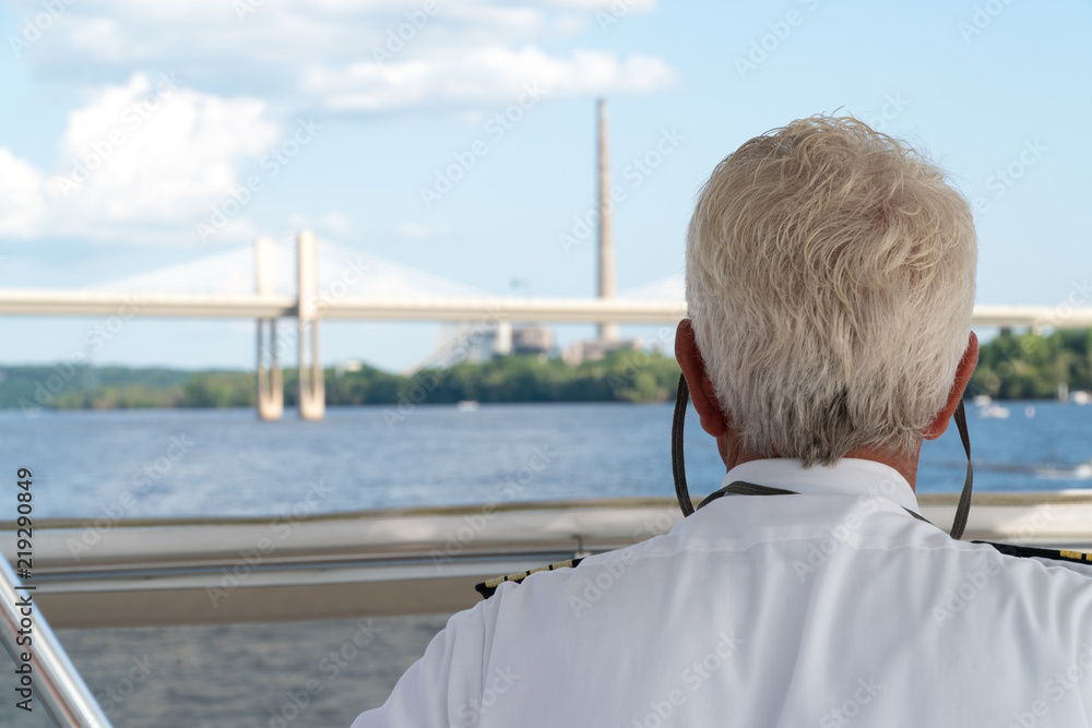 Fototapeta premium Over the shoulder POV view of a boat captain sailing down a river. Charting navigation path under bridge and past smoke stack factory on a clear summer day