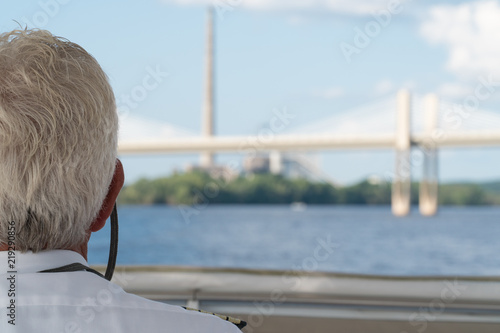 POV over the shoulder view of boat captain sailing down a river towards highway bridge overpass during day time. Navigation to check water depth for nautical safety